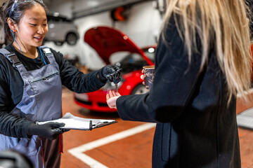 Female mechanic delivering car key to customer in repair shop