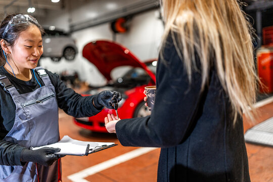 Female mechanic delivering car keys to customer in auto repair shop