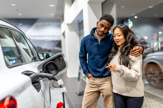 Young couple choosing eco friendly vehicle at electric car dealership