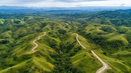 Aerial view of a winding mountain road cutting through lush green hills under a clear sky. No people included.