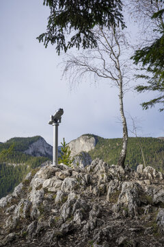 A Rocky Mountain Peak With A Binocular On The Top Surrounded By Trees, Mountains And Overcast Sky In The Background
