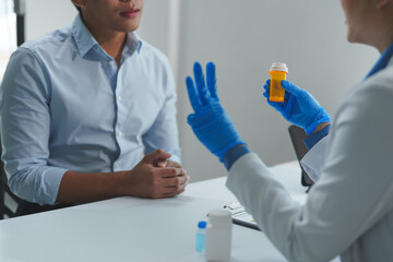 Medical doctor wearing blue surgical gloves is showing medicine bottle and explaining dosage to...