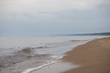 
a sandy beach with waves lapping against the shore and a slightly overcast sky above the horizon.