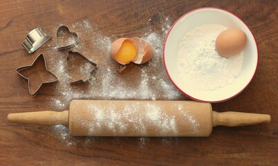 Rolling wood with baking ingredients, flour, eggs, cookie cutters on wooden board