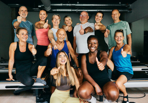 Smiling group of diverse men and women in sportswear giving the thumbs up together after an exercise class in a pilates gym - Powered by Adobe