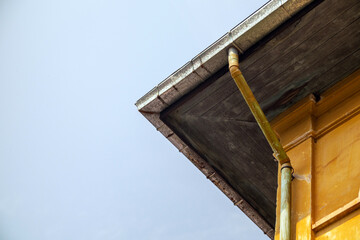 Obraz premium A striking perspective of a renovated building showcasing a galvanized roof, yellow-painted rusted pipes, and architectural elements that contrast modern and aged materials.