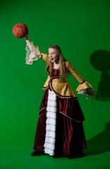 Obraz premium Woman in ancient outfit on chroma key green screen background. Female in renaissance dress with excited face holding basketball ball in hand ready to throw.