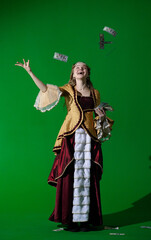 Fototapeta premium Woman in ancient outfit on chroma key green screen background. Female in renaissance dress with happy smiling face throwing money dollars banknotes in the air.
