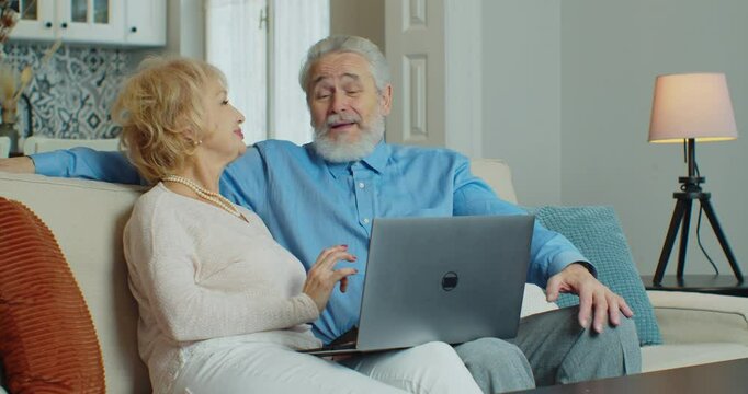 Old retired couple using laptop doing internet shopping choose sale offers together, senior elderly family grandparents relaxing looking at computer screen sit on sofa at home. Coronavirus quarantine