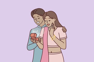 Indian man surprises wife with box of jewelry or engagement ring as token of love and devotion. Guy and girl in Indian national costumes during romantic date or engagement ceremony