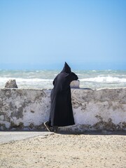 A Berber with black djellaba leaning against the harbor wall, Place Moulay Hassan, Essaouira,...