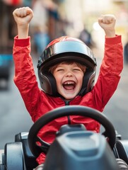 Naklejka premium Happy laughing boy raising hand in victory after riding gokart outdoor. KId having fun and driving toy race car on street. Child exult while riding an electric or peddle toy auto wearing pilot helmet