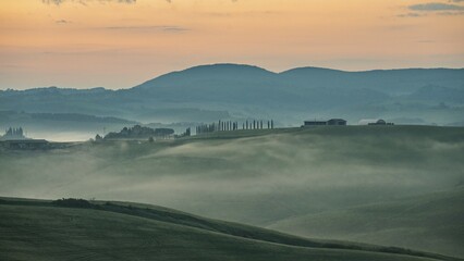 Fototapeta premium Hilly landscape with foggy atmosphere and country estate, morning light, Tuscany, Siena province, Italy, Europe