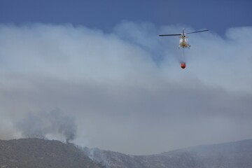 Helicopter flies with an extinguishing water tank to a fire, Los Molles, La Ligua, Valparaíso,...