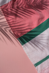 Fototapeta premium Colorful striped cotton beach towel on the pink background with palm leaves shadows. Copy space