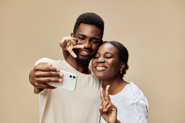Happy young couple taking a selfie together against a warm beige background, showcasing love and...