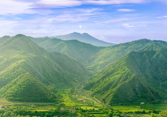 Obraz premium amazing view at a green landscape between two mountains with a high peak with snow and blue cloudy sky on background