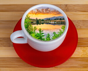 a cup of coffee or tea with beautiful evening lake sunset landscape inside, travel or nature concept