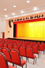 A spacious auditorium filled with empty red chairs and yellow curtain.
