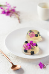 Berry jelly with blueberries and flowers ivan tea on white plate. Vertical orientation.