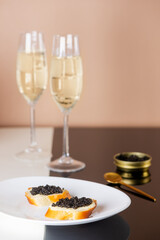 Sandwiches with black caviar with glasses of champagne on a table. Sturgeon caviar. Vertical orientation.