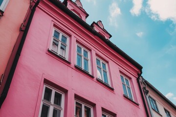 Obraz premium Bright pink building with classic architecture and clouds in the background captured during the day in a vibrant urban neighborhood