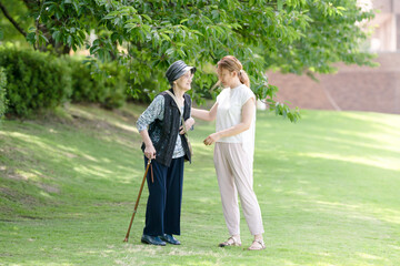 Fototapeta premium At grass area of A park with good atmosphere with canal in Toyama Prefecture. Old woman in her 90s and Japanese woman in her thirties are walking around the park.