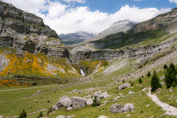 A scenic mountain valley with a waterfall, surrounded by rugged cliffs and alpine meadows in Ordesa y Monte Perdido National Park, Spain. A perfect location for trekking, hiking, mountaineering, and s