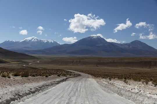 Gravel road leads through Altiplano, behind snow covered volcanoes, near Colchane, Tarapaca, Chile, South America
