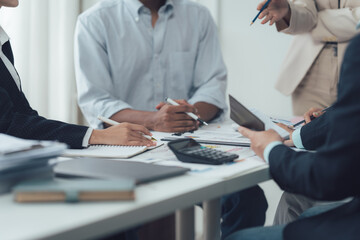 Strategic Collaboration: A close-up shot of a diverse team engaged in a collaborative meeting, their hands reaching for pens and calculators as they analyze data and strategize for success.