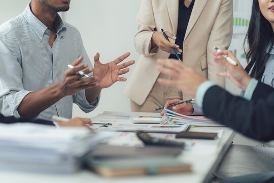 Business Team Brainstorming: A diverse group of professionals actively engaged in a collaborative meeting, sharing ideas and strategies around a table filled with documents and office supplies.
