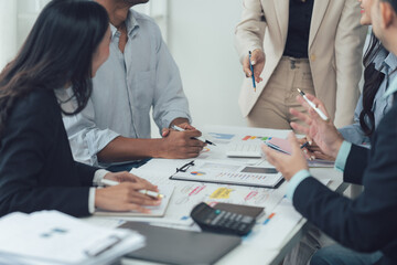 Fototapeta premium Collaborative Business Meeting: A diverse team of professionals gathers around a table, engaged in a lively discussion over financial charts and reports.