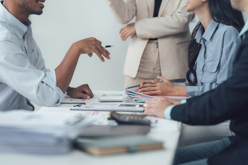 Strategic Business Meeting: A diverse team of professionals engages in a collaborative discussion around a table, reviewing financial documents and charts.