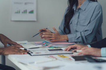 Strategic Business Meeting: A diverse team of professionals engages in a collaborative discussion around a table, reviewing financial documents and charts.