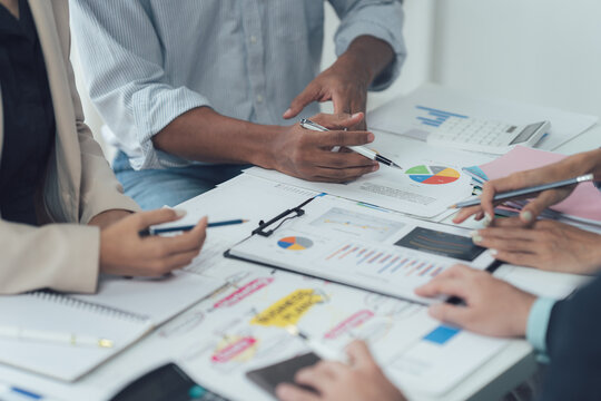 Strategic Business Meeting: A diverse team of professionals engages in a collaborative discussion around a table, reviewing financial documents and charts.