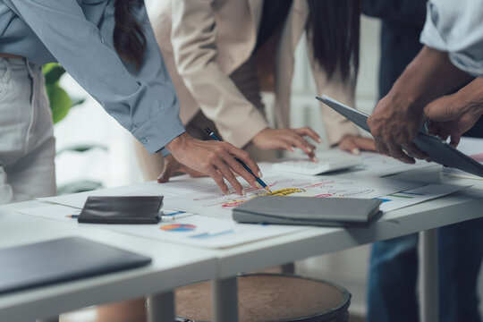 Collaborative Business Strategy Session: A close-up shot showing a team of diverse business professionals leaning over a large table.