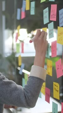 Asian Business Woman Write Tasks Creative Ideas On Sticky Notes On Glass Board, Female Corporate Leader Planning Project On Post It Sticky Notes Organize Work On Stickers