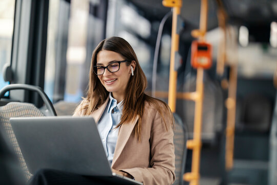 Happy woman in suit sitting in public bus with laptop and smiling at it. - Powered by Adobe