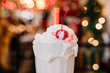 A melting milkshake with whipped cream and cherry in a festive café.