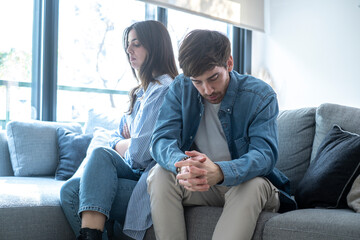 Sad and emotionally distant couple sitting apart on a sofa in a home interior, struggling with...