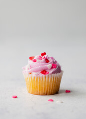 Close up of cupacke with pink frosting and hearts on white background.