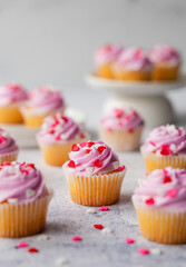 Small cupackes with pink frosting and hearts on white background.