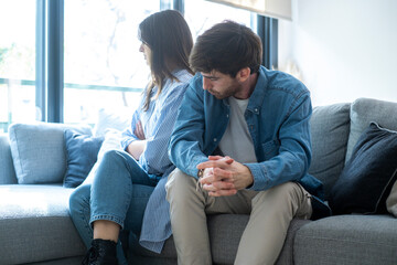 Millennial couple sitting on the couch at home, facing away from each other, struggling with love...
