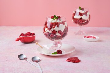 Dessert, trifle Red velvet with butter cream and raspberries in glasses on pink concrete background with Valentine's Day decor. Dessert for lovers. Portion desserts.