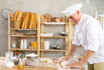 Elderly man baker rolls out dough