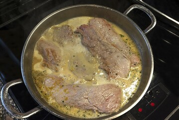 Meat cooks in sauce in a pan on the stove