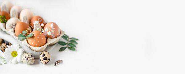 A delicate Easter background with hand-painted eggs in a box on a white table. Easter composition with flowers and feathers