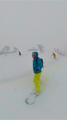 SELFIE, VERTICAL: A snowboarder carves effortlessly through deep snow in a serene alpine forest in...