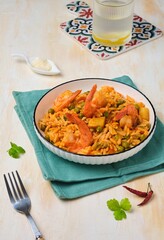 Orzo pasta with carrots, green peas and shrimps with tomato sauce in a white plate on a light concrete background. Seafood recipes.