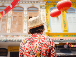 Naklejka premium Young woman in ethnic dress and hat exploring the vibrant streets of Malacca, Malaysia. A blend of cultural heritage, colorful architecture, and tropical charm. Perfect travel and lifestyle moments.